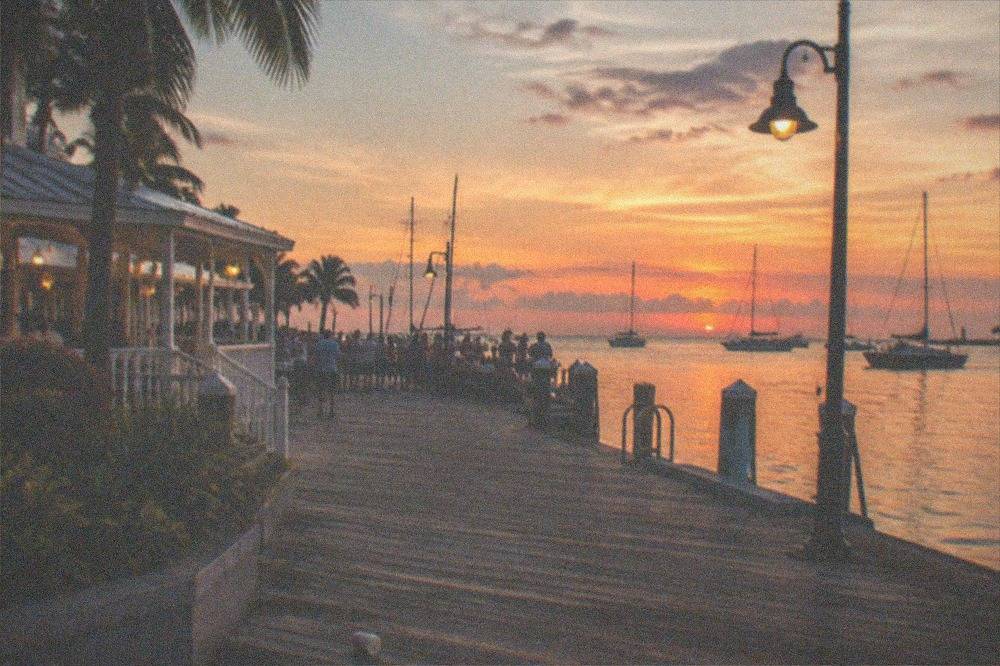 Waterfront square in Key West at dusk with boats in the harbor and street lamps glowing