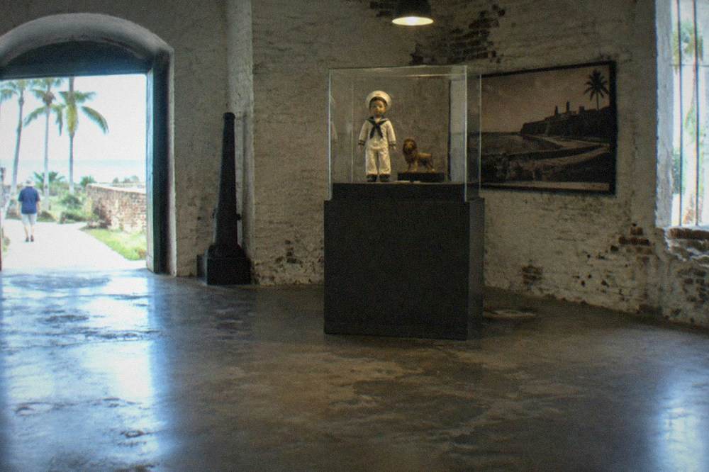 Old sailor-suited doll displayed in a glass museum case beside a small lion figure