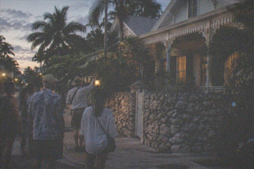 Lantern-lit evening walking tour group paused on a historic Key West street corner