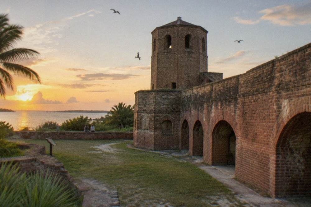 An old brick fort turret and walls overlooking water under an evening sky