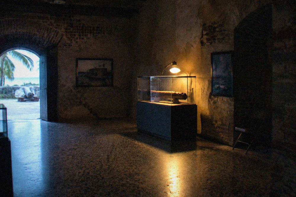 A dark museum gallery interior with an empty display case lit by a single lamp