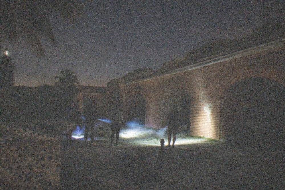 A dimly lit fort courtyard at night with a small group holding flashlights