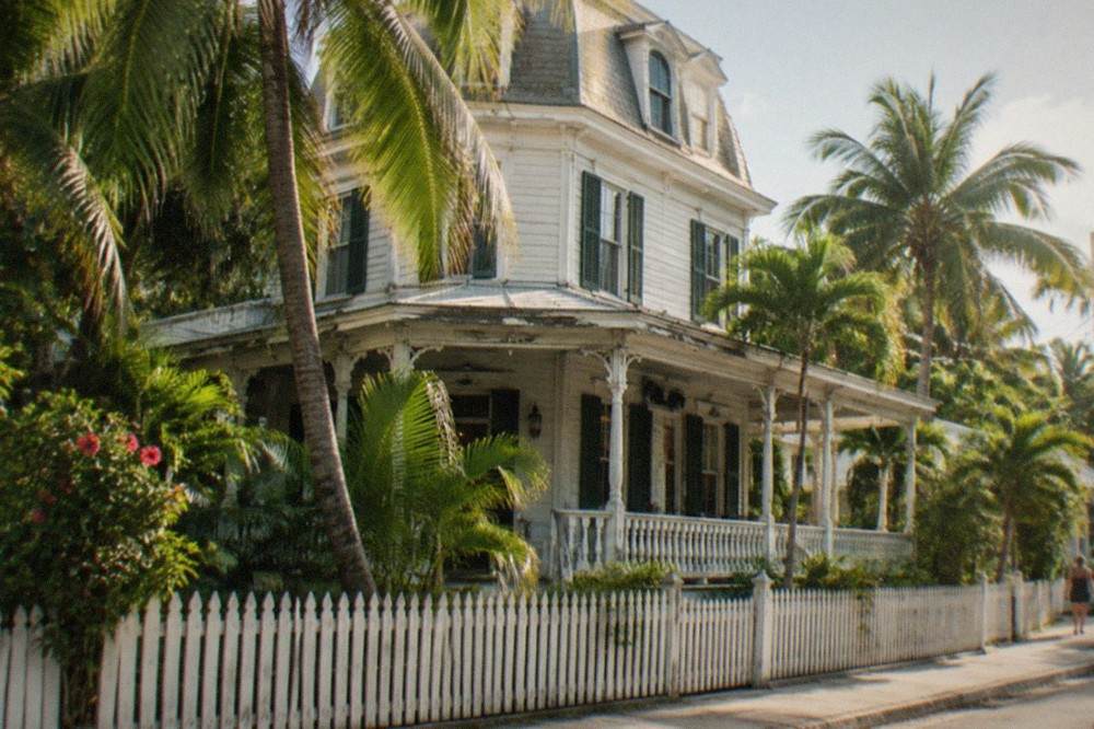 A wooden Victorian house with a front porch under palm trees