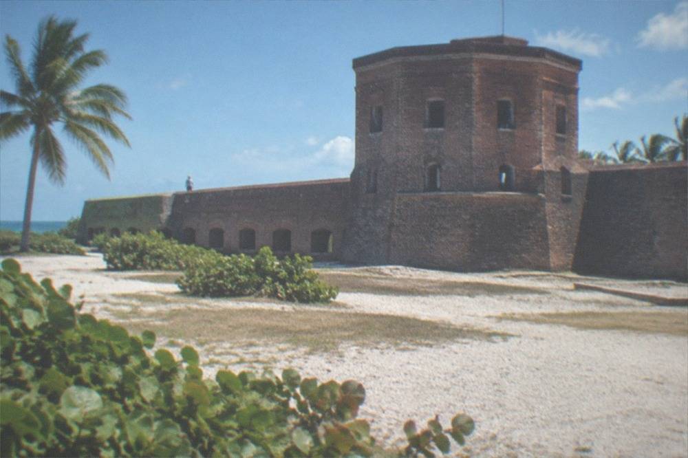 A historic fort tower and open grounds under a bright sky