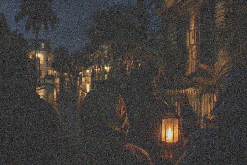 A lantern-lit walking ghost tour group paused on a Key West street at night