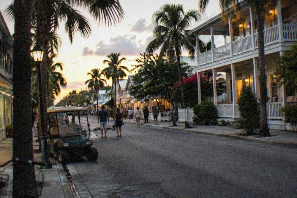 A busy Duval Street block in Key West at dusk with lit shopfronts and palm trees along the sidewalk