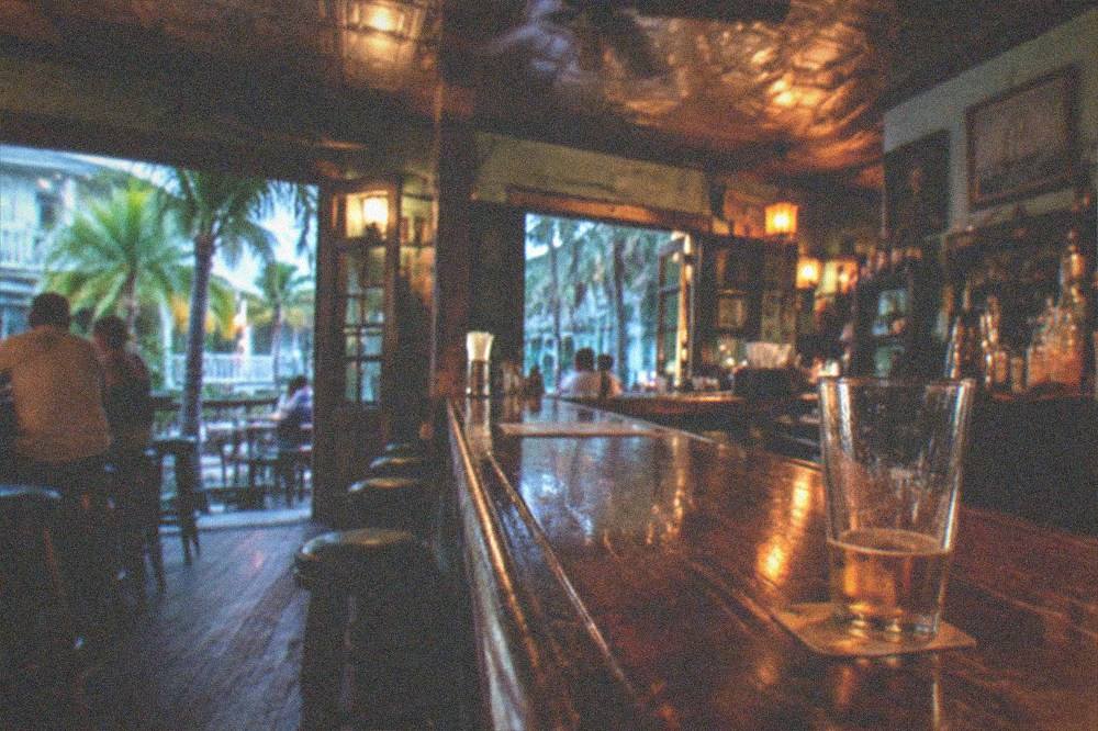 The interior of a historic Key West bar at night with warm lamplight reflecting off a long wooden counter