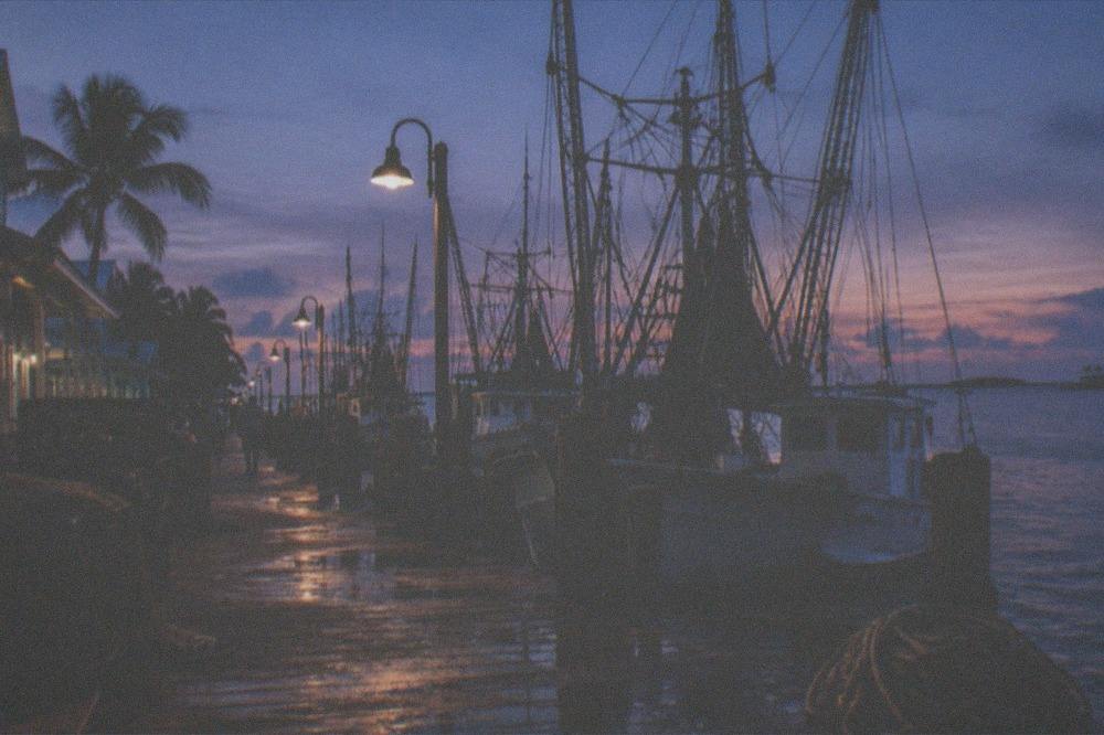 The Key West waterfront at dusk with masts, lampposts and a darkening sky over the harbor