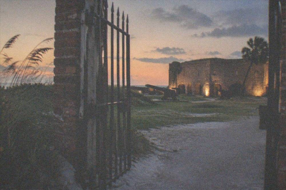 Open gate of a brick Civil War fort at dusk with lights beginning to glow