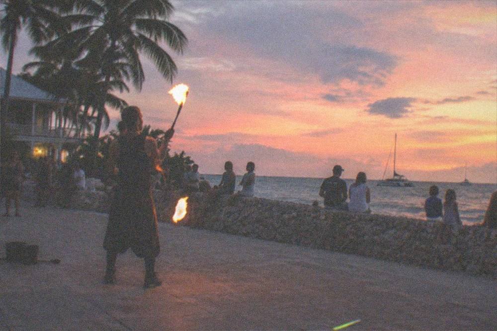 Street performer juggling fire for a crowd of families on the Mallory Square seawall at dusk