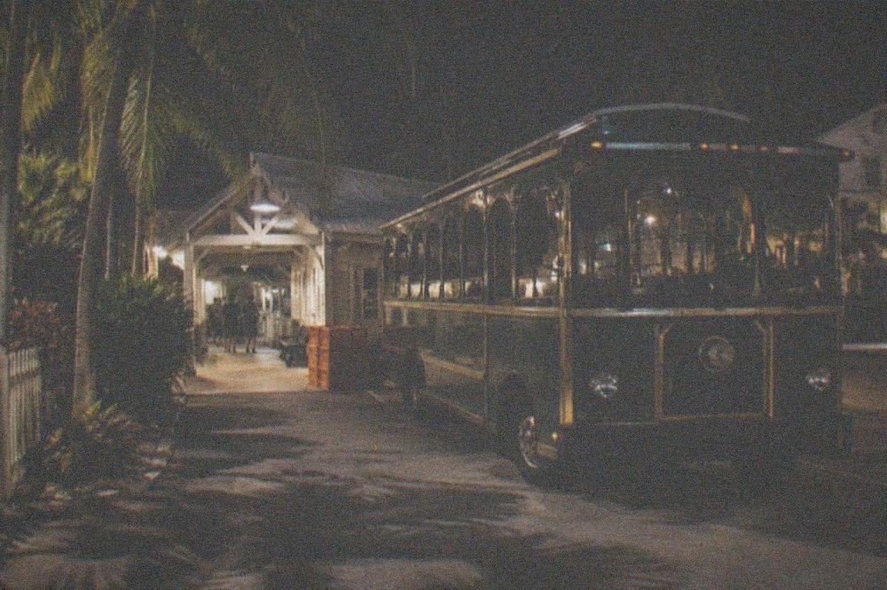 Vintage-style ghost tour trolley parked on a lamplit Key West street at night