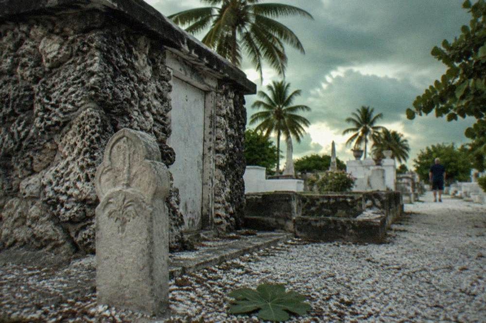 A close view of carved headstones and an above-ground family crypt along a sandy lane in Key West Cemetery