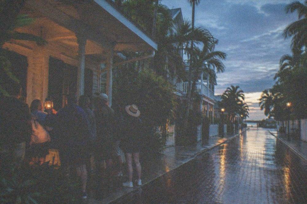A guided walking group gathered at dusk on a lamplit Old Town street in Key West