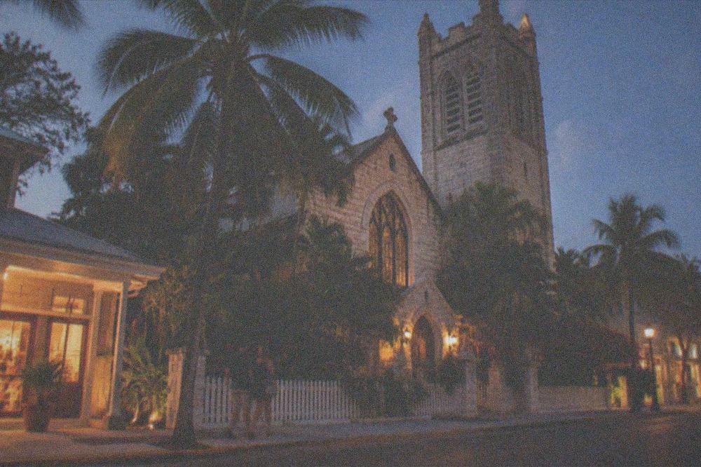 An old church facade and lit storefronts along Duval Street after dark in Key West