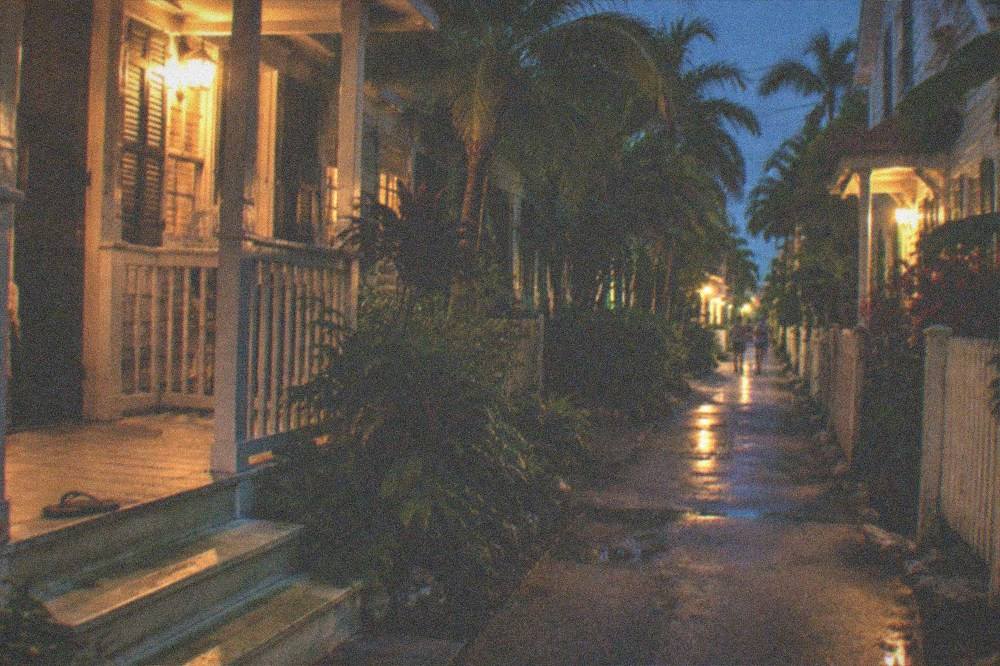 A narrow lamplit lane between old wooden Key West houses at night