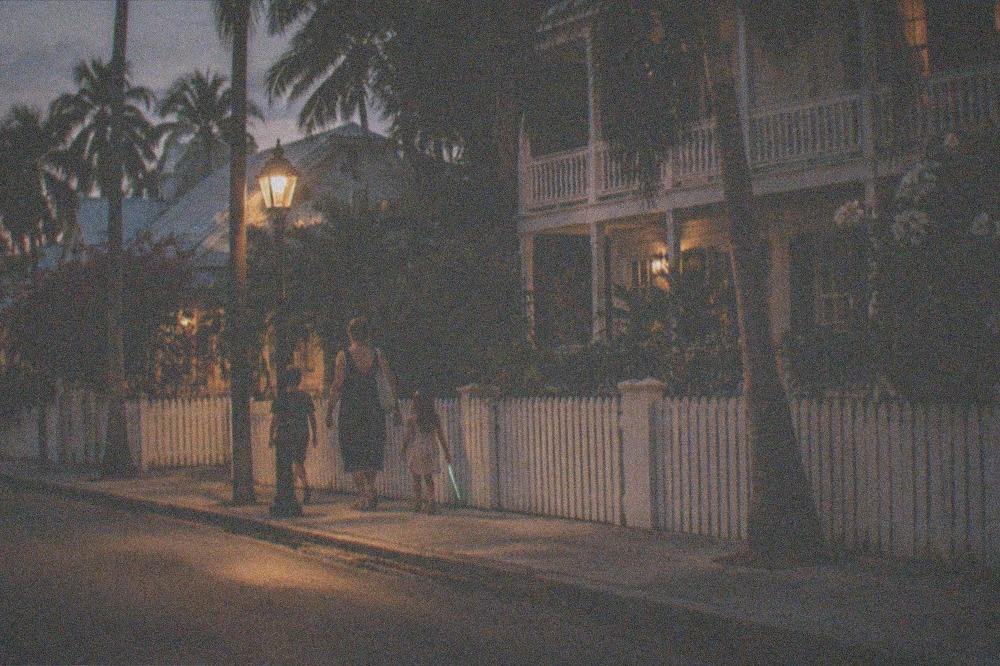 A parent and two children walking a lamplit sidewalk in Old Town Key West