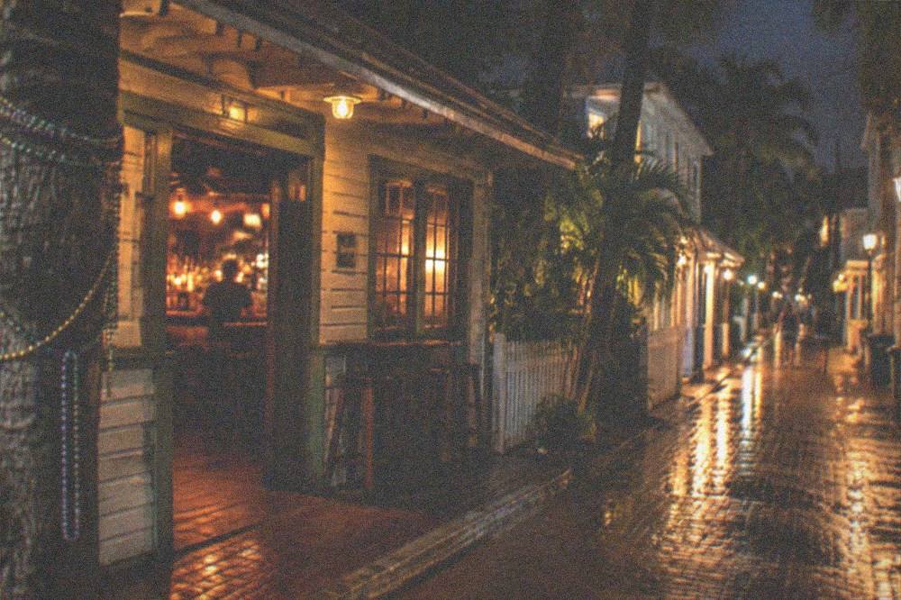 A historic Key West bar exterior at night with warm light spilling onto the sidewalk