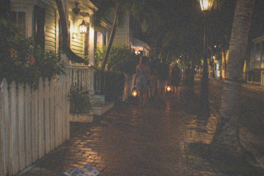 A candlelit tour group walking past illuminated historic Key West facades at night