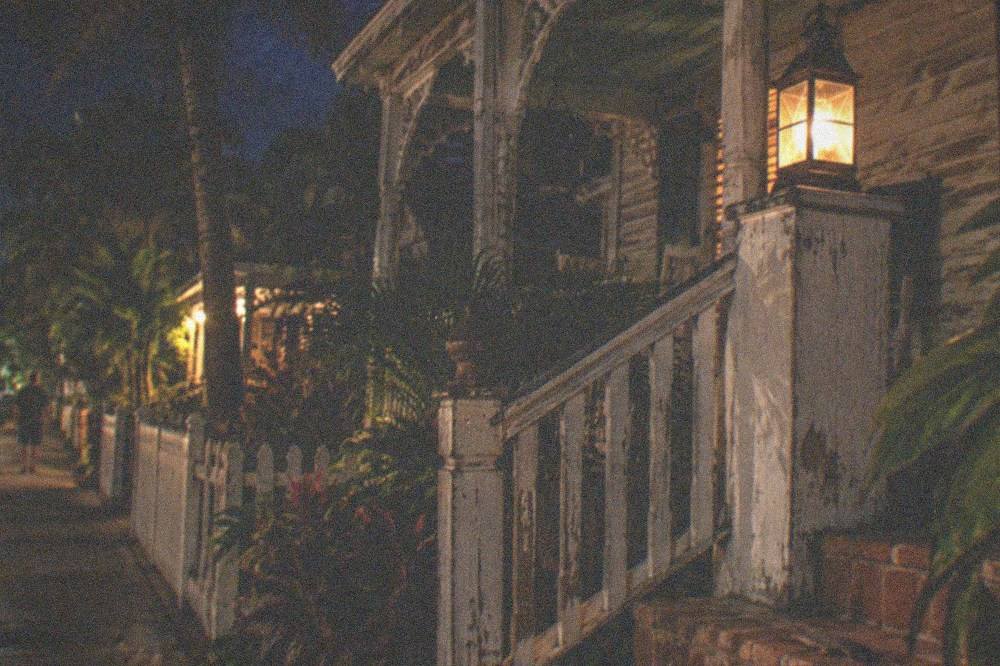 A lantern glowing on a wooden porch of an old Key West guesthouse at night