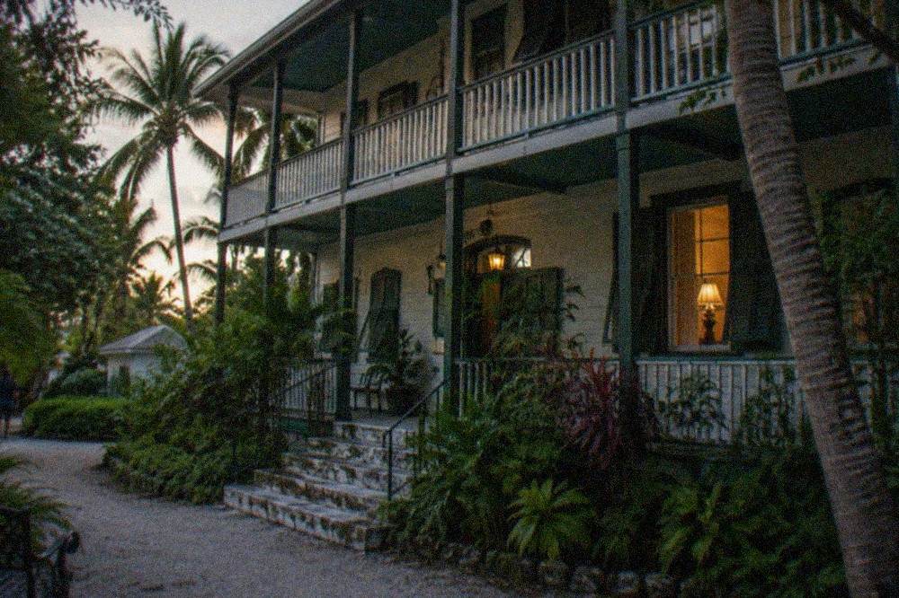 Historic wooden Key West house with a deep porch lit by evening lamps
