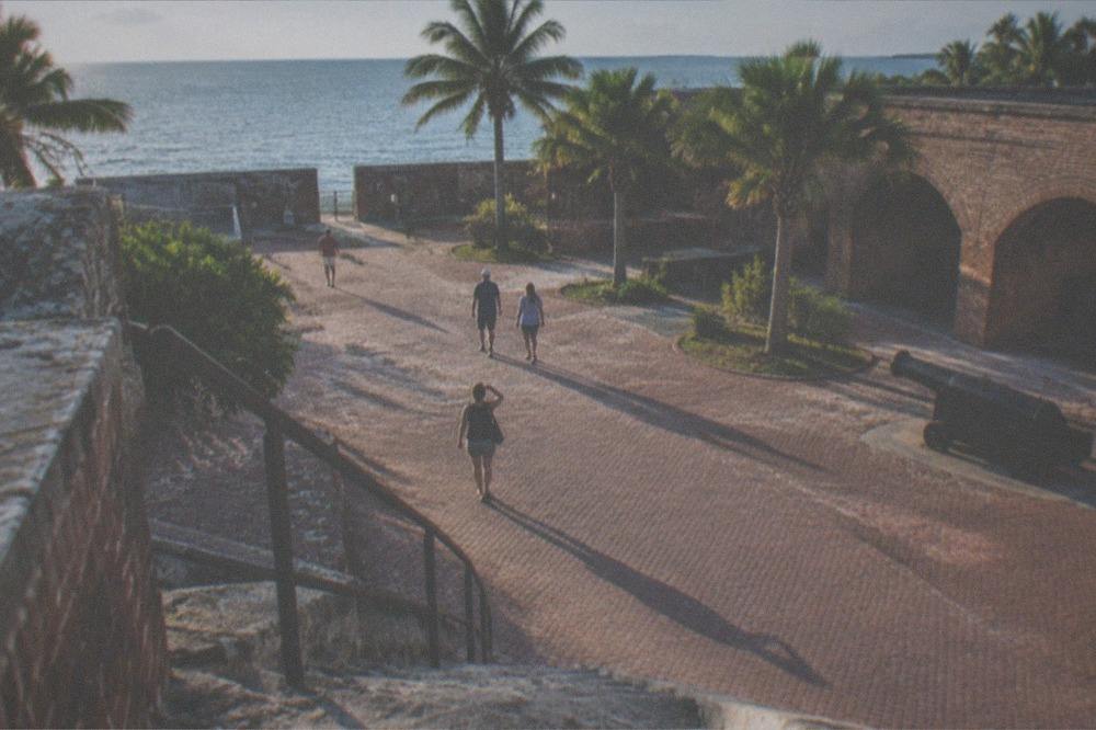 Visitors walking through a brick fort courtyard toward a museum entrance