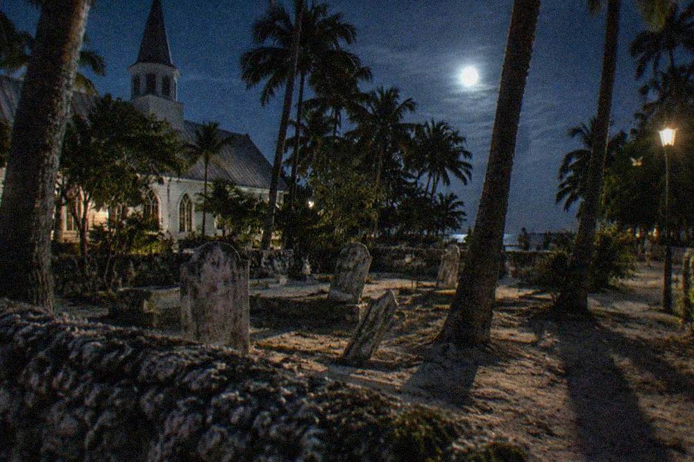 St Paul's Episcopal Church graveyard at night with old headstones and palm shadows across the wall