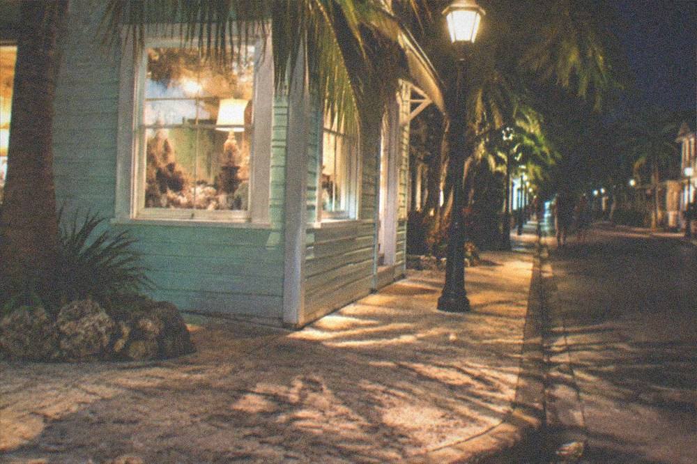 A quiet Key West corner at night with a lit storefront sign and empty sidewalk