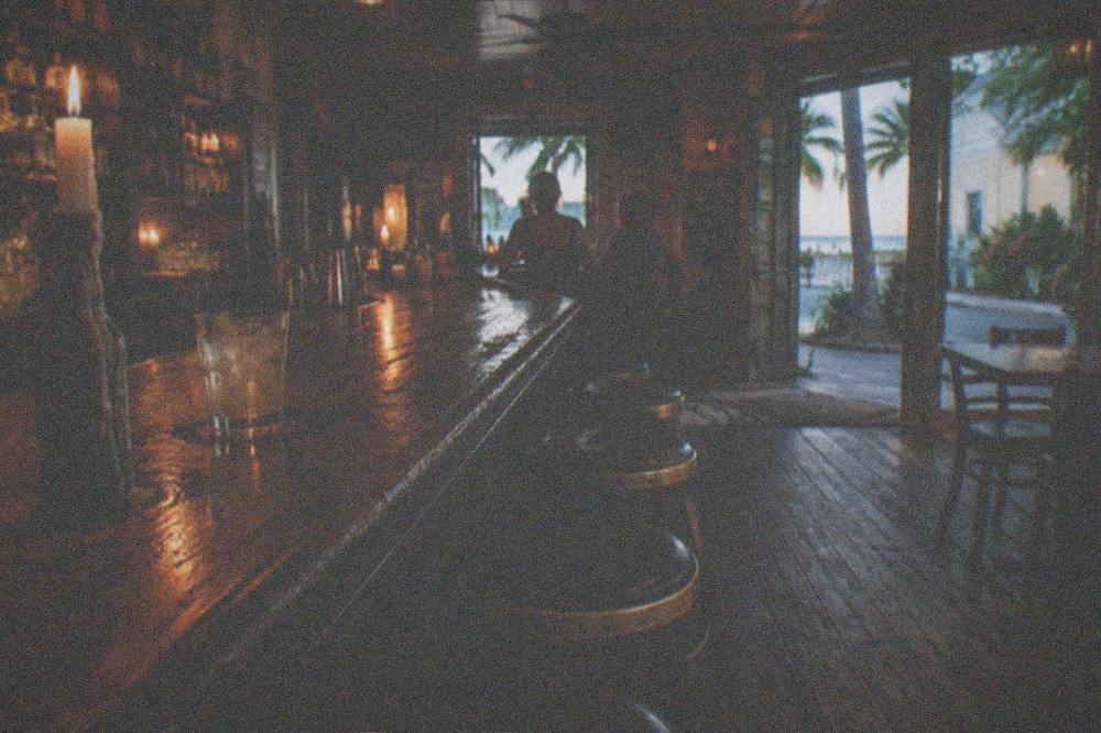 A candlelit bar interior in Key West at night with stools and a worn wooden counter